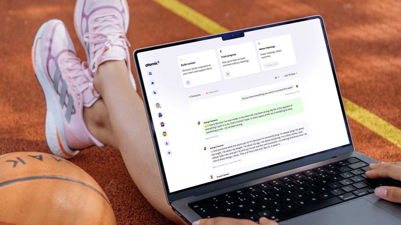 Atomic8 web app open on a laptop on a running track, showing a team dashboard with chat messages