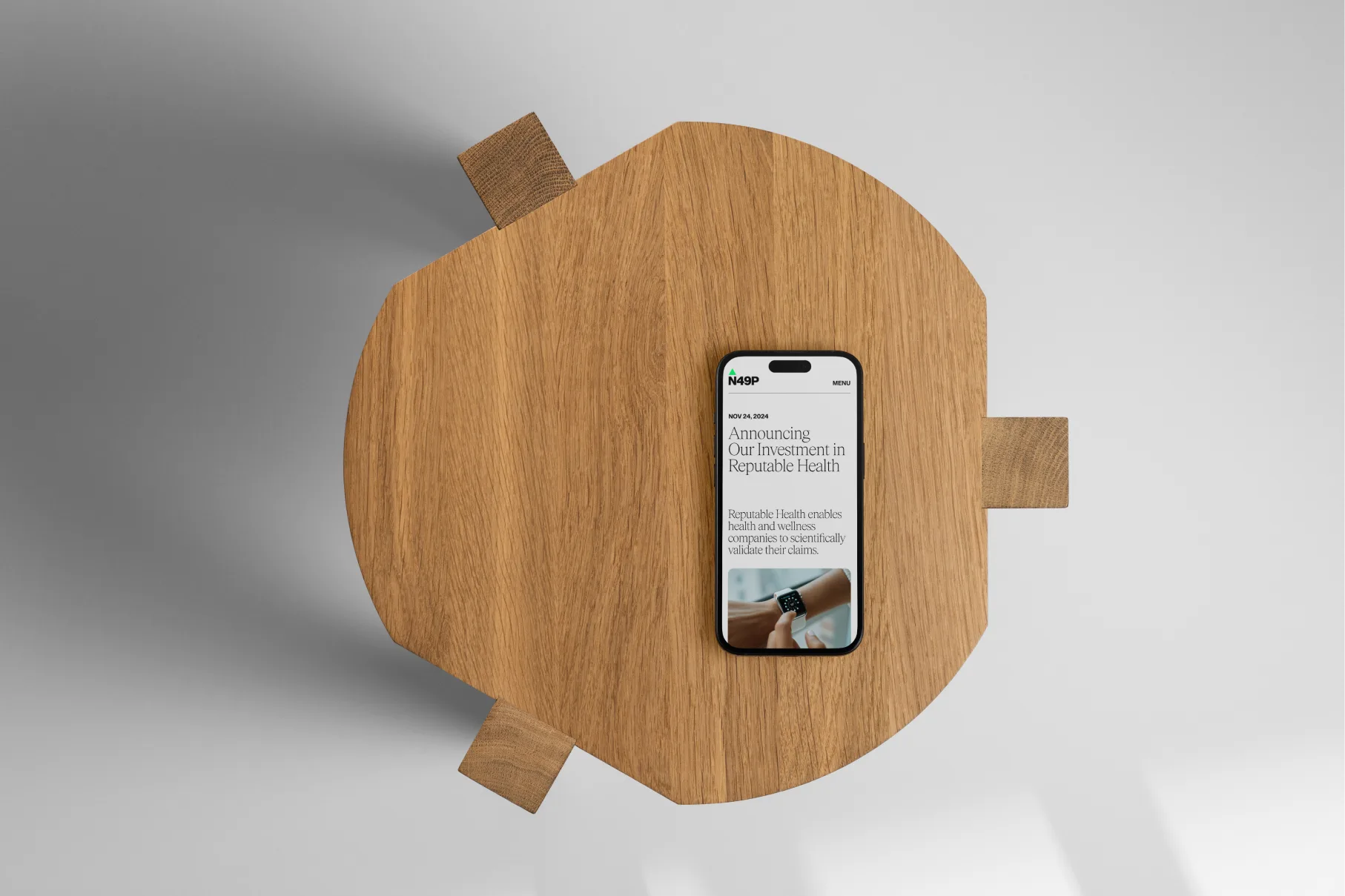 N49P website on a phone, top-down on a wooden table, showing the article 'Announcing Our Investment in Reputable Health'